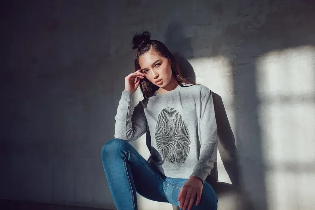 PSD Mockup Sweatshirt Apparel Design, Woman wearing gray sweatshirt with fingerprint design sitting against wall